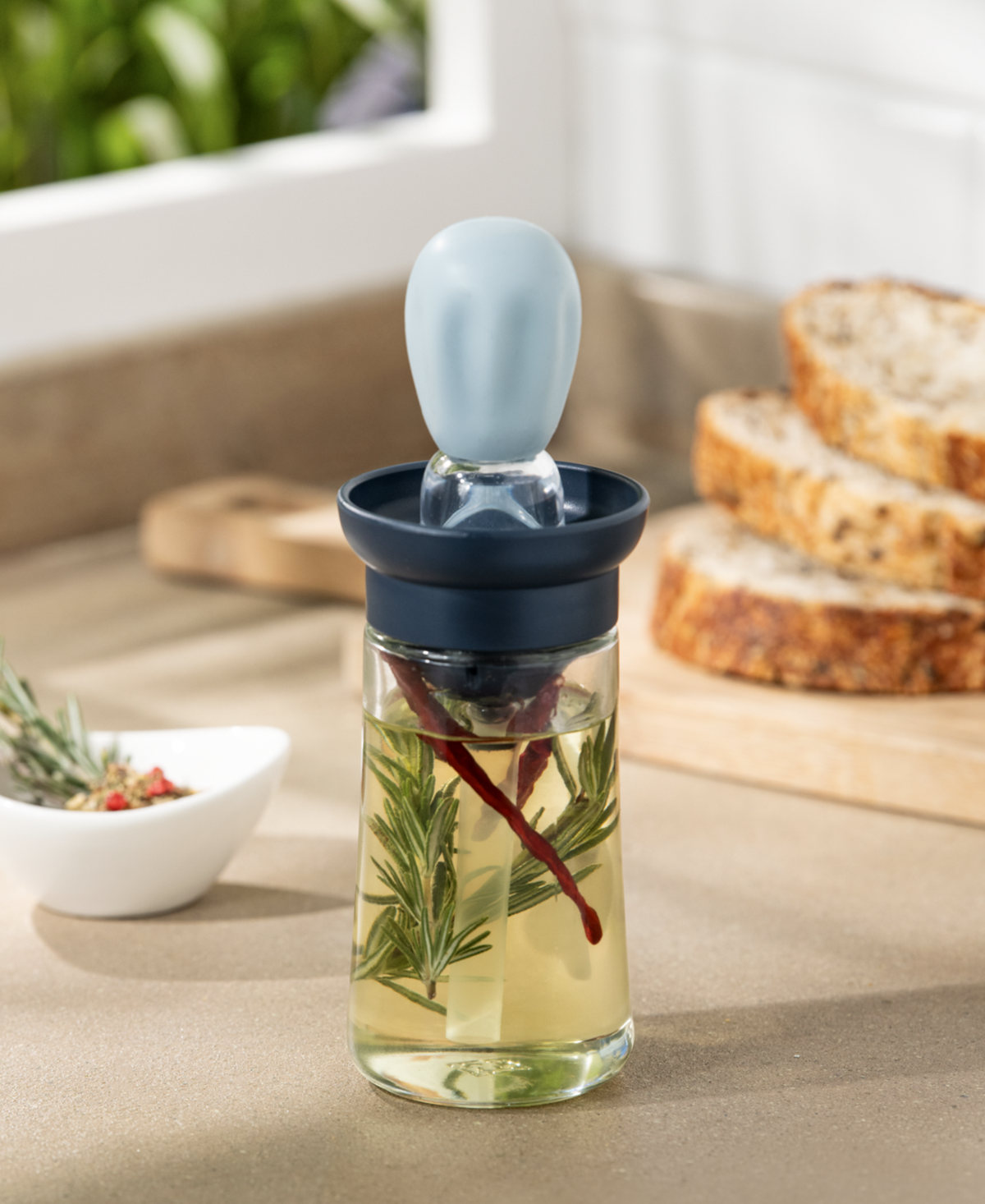 Oil dispenser with rosemary beside bread, near a window