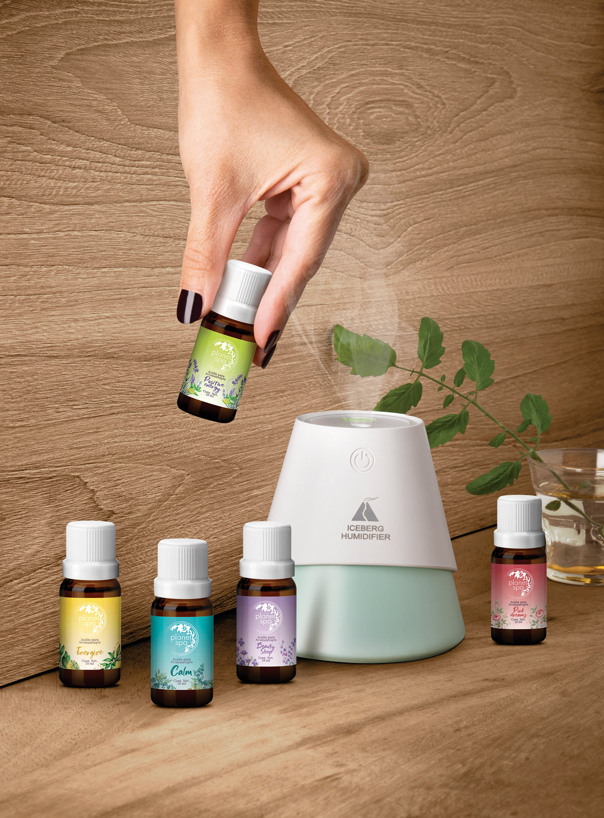A hand holds an essential oil bottle over a diffuser, with bottles on wood