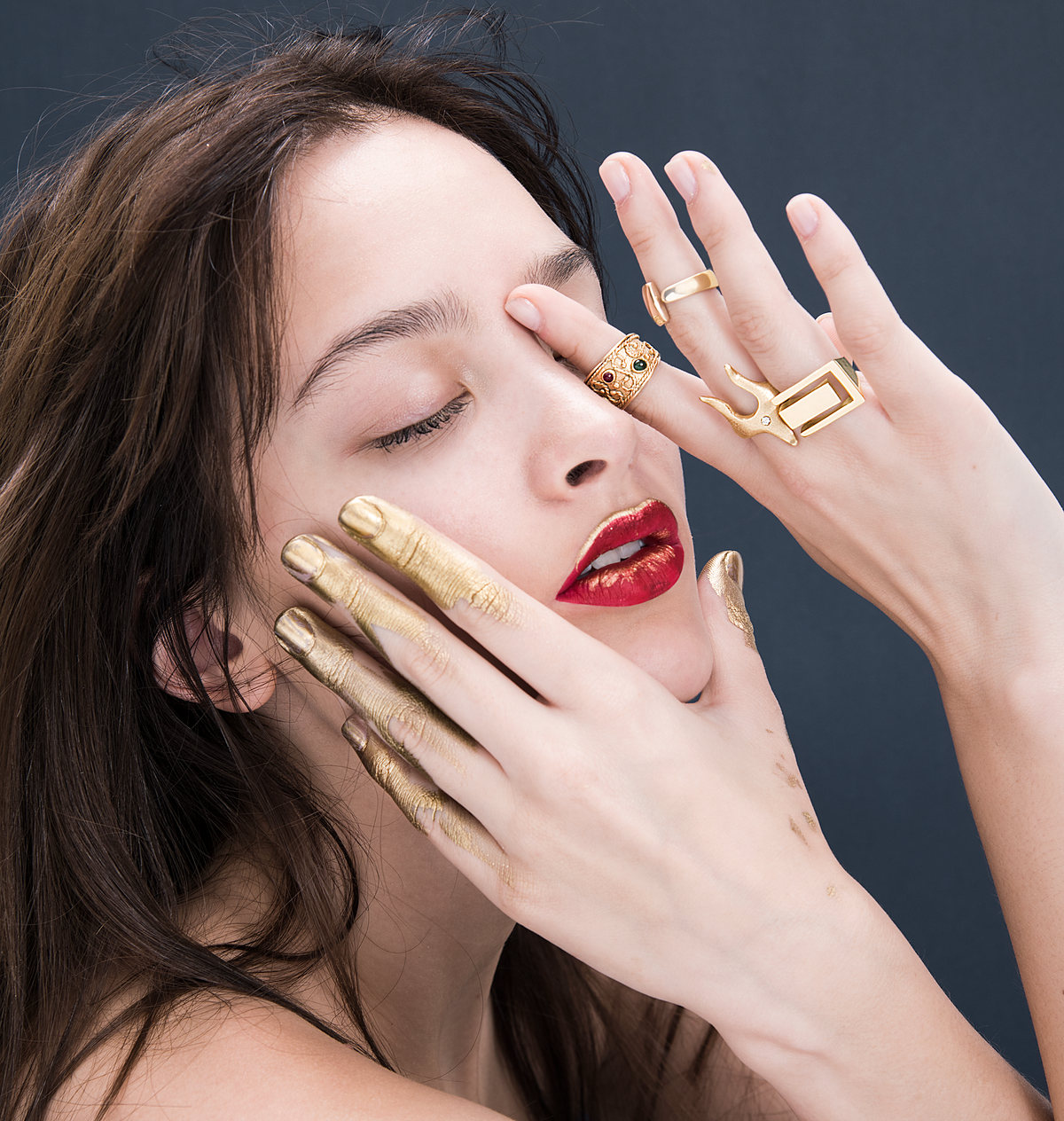 Model with eyes closed, a hand with gold rings resting on her face