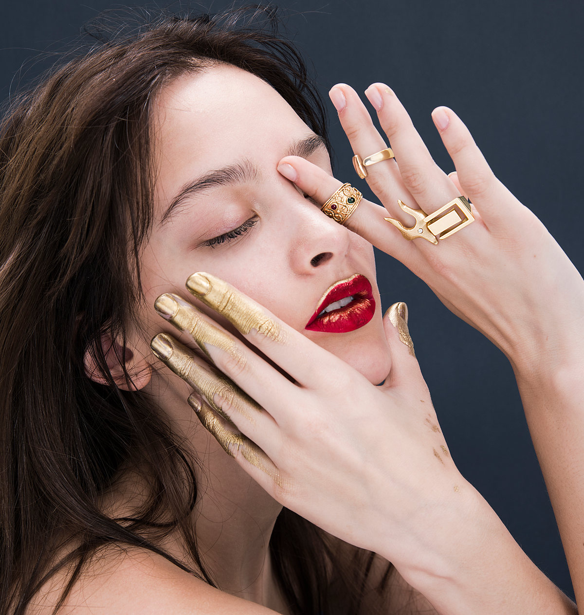 Modelo con los ojos cerrados y la mano con anillos dorados sobre el rostro