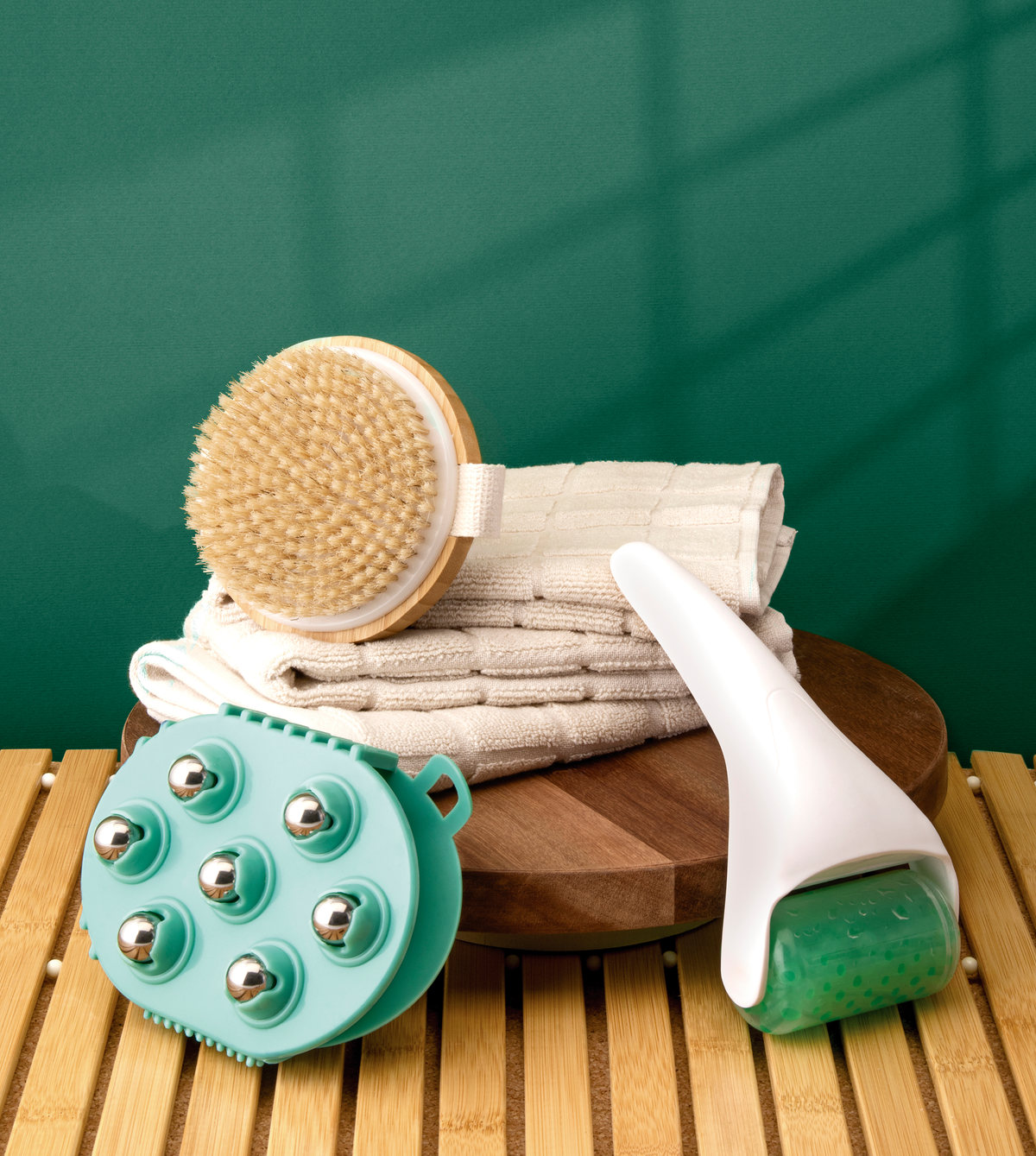 Bath brush, massager and face roller on towels and bamboo against green