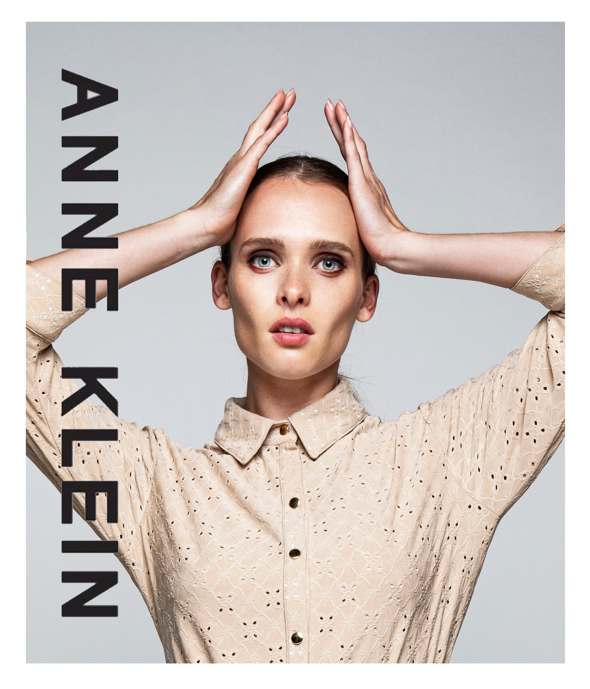 Modelo con blusa calada beige y las manos en la cabeza, con logotipo de Anne Klein