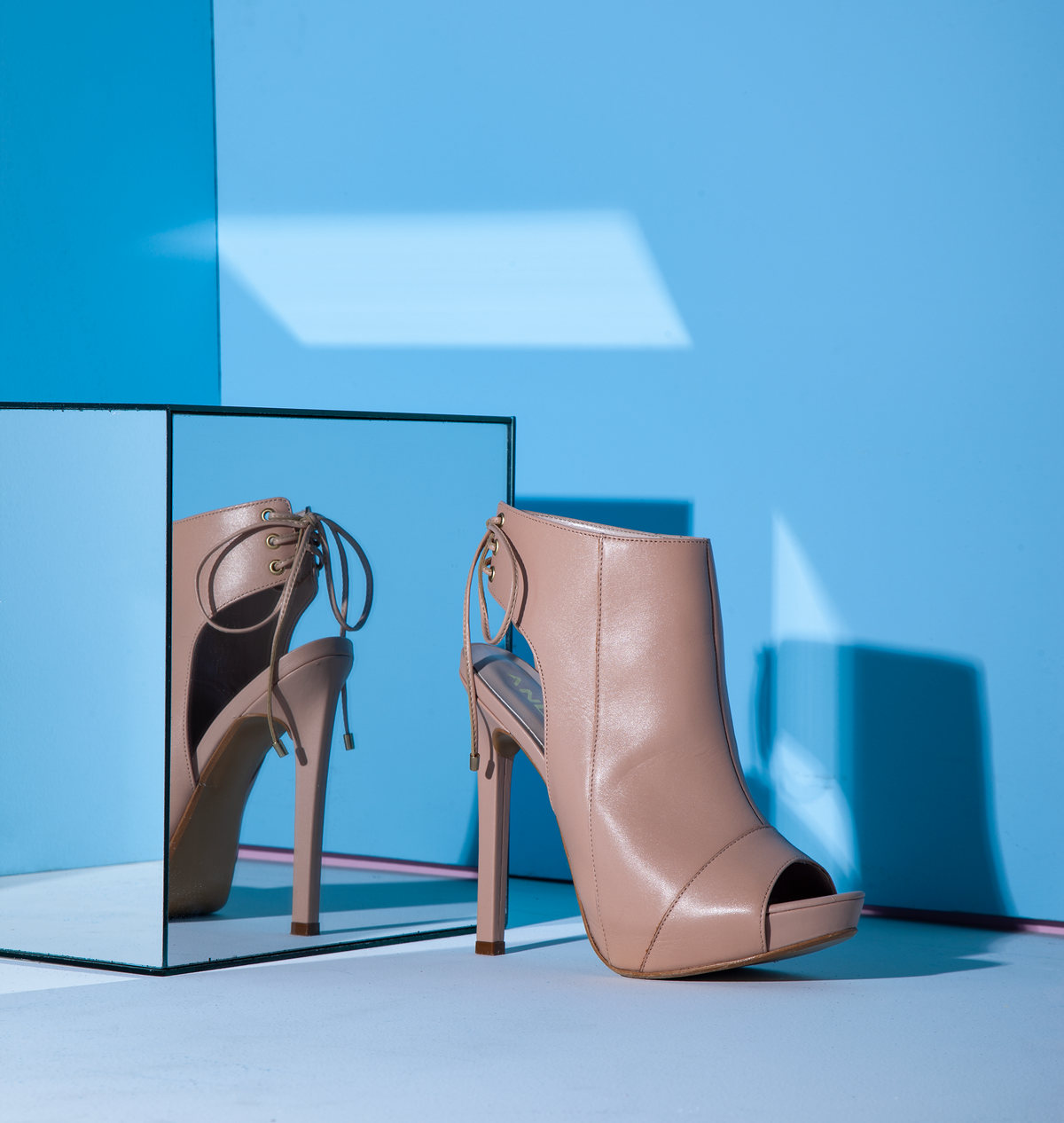 Botines de tacón color nude sobre una caja de espejo con fondo azul