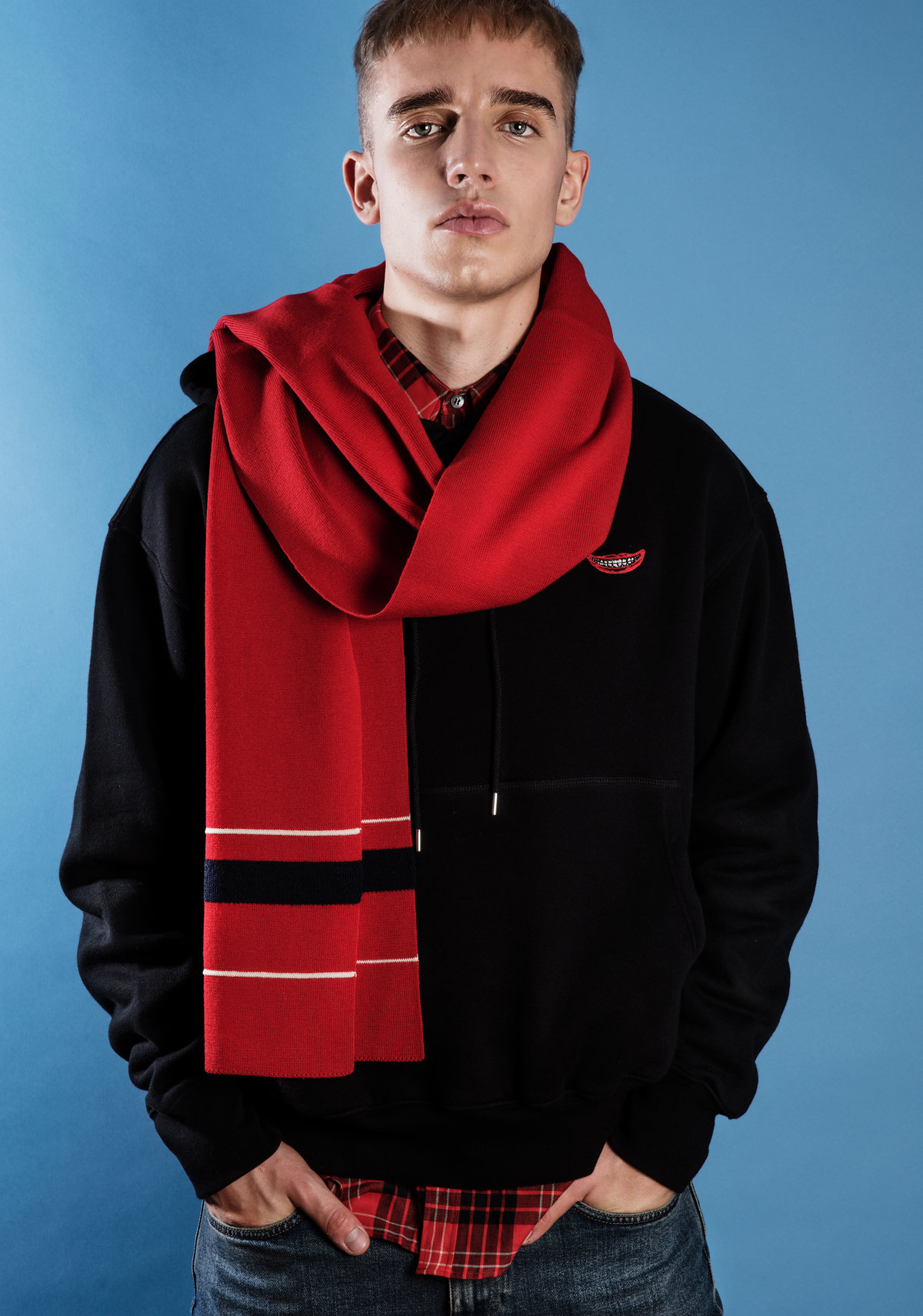 Modelo con bufanda roja y sudadera negra sobre fondo azul