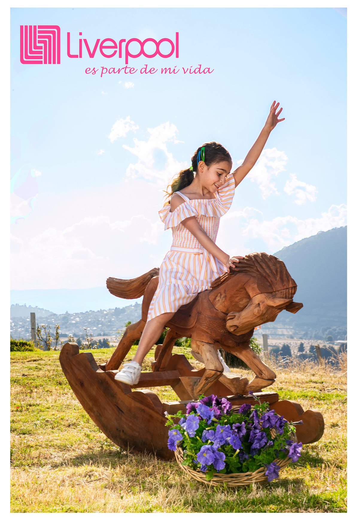 Niña sobre un caballito de madera en un jardín con montañas al fondo, con logotipo de Liverpool