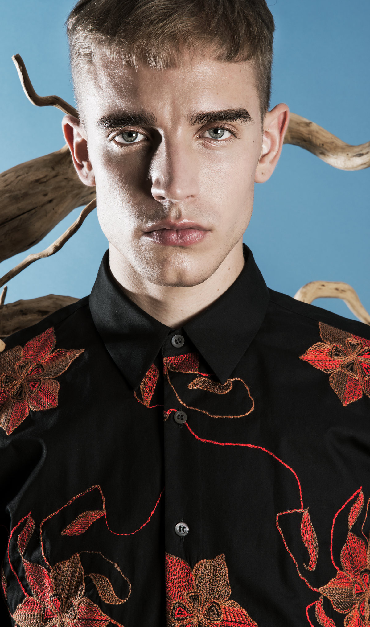 Retrato de modelo con camisa negra de flores rojas sobre fondo azul con ramas