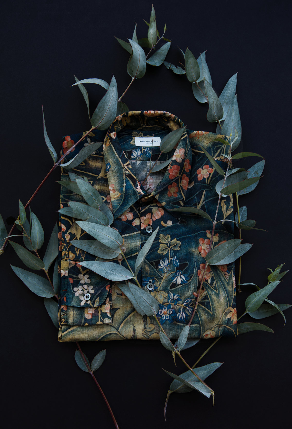 Camisa de estampado floral rodeada de ramas de eucalipto sobre fondo negro