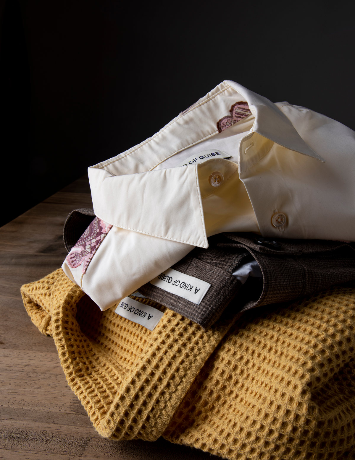 Camisas blancas dobladas sobre un suéter mostaza en una mesa de madera