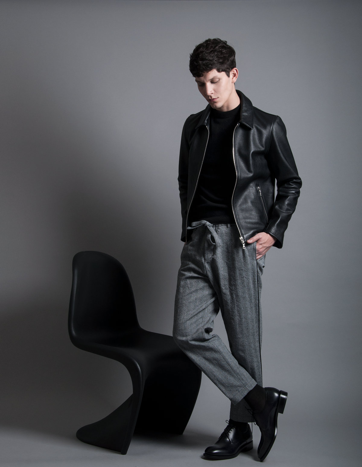 Modelo con chamarra de piel negra y pantalón gris junto a una silla negra