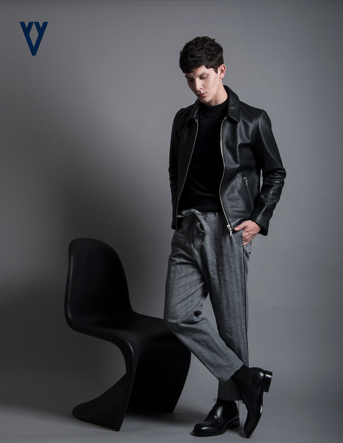 Modelo con chamarra de piel negra y pantalón gris junto a una silla negra, con logotipo de The Silver Deer
