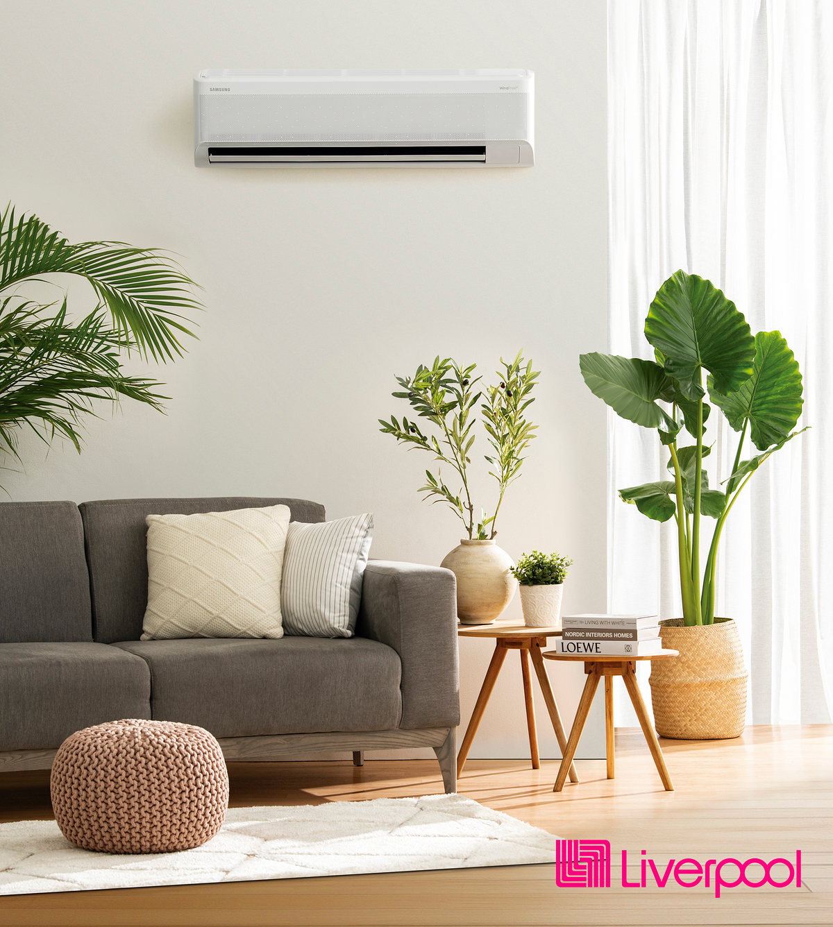 Bright living room with a wall-mounted air conditioner, gray sofa and plants, with the Liverpool logo
