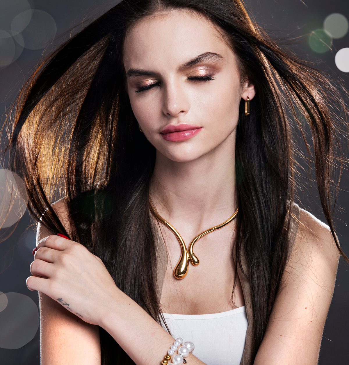 Model with eyes closed and hair in motion, wearing a sculptural gold necklace