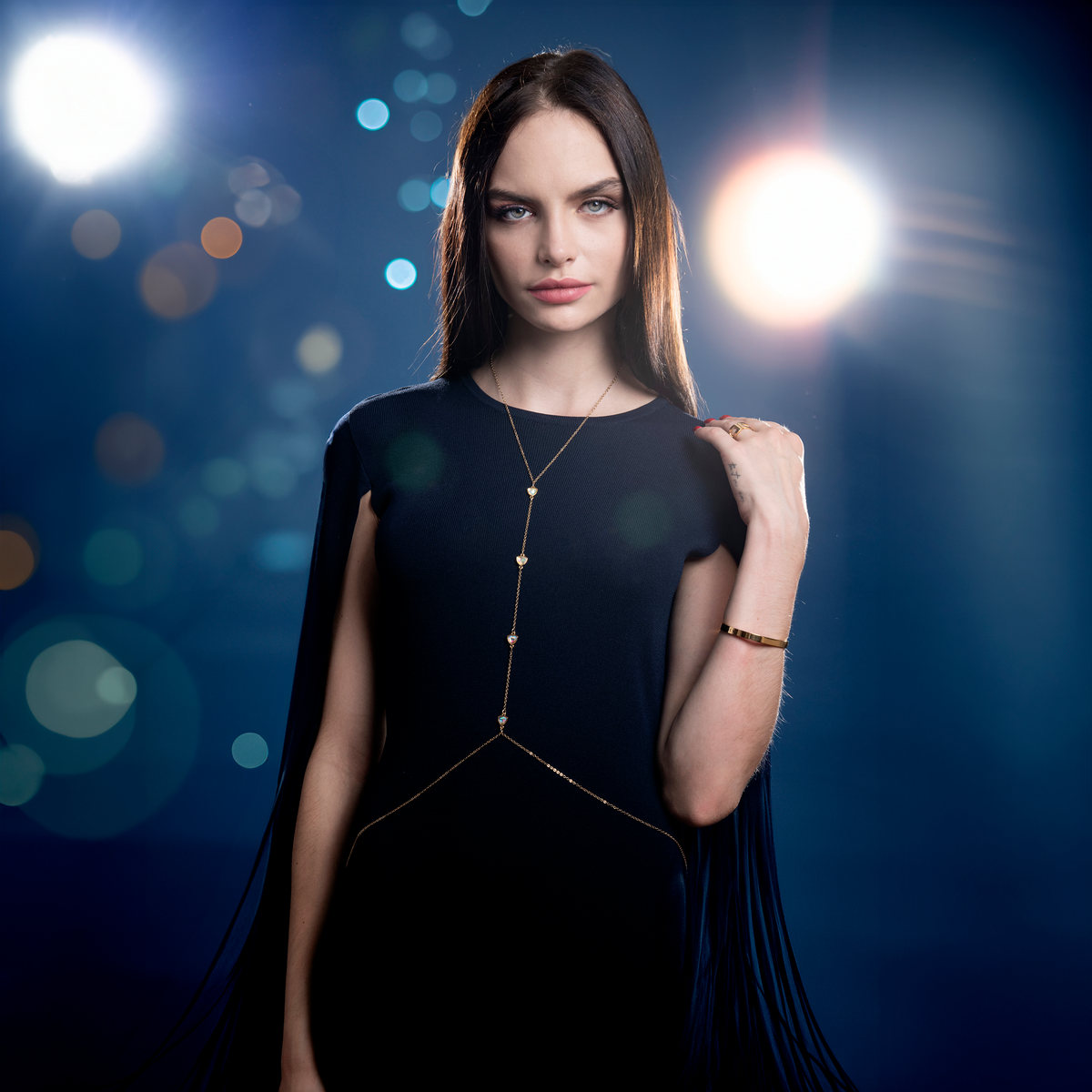 Model in a black dress with a gold body chain before out-of-focus blue lights