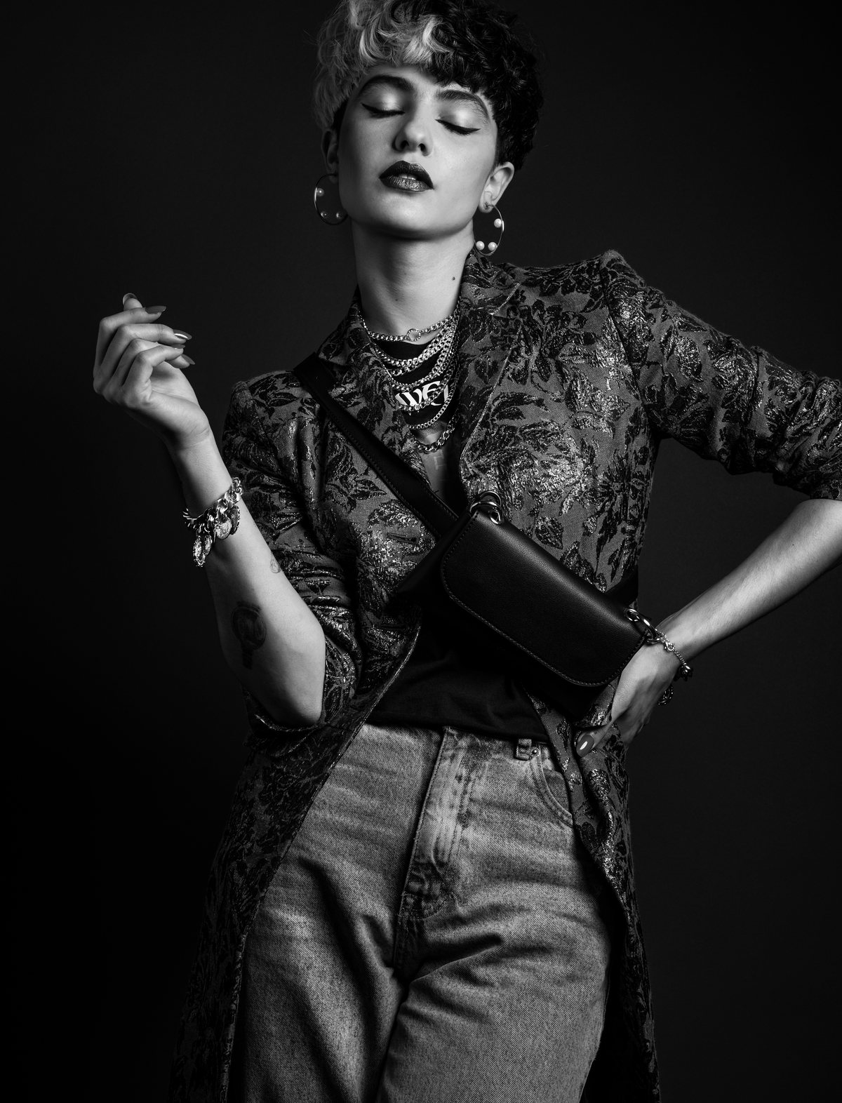 Black-and-white image of a model in a lace jacket, necklaces and jeans