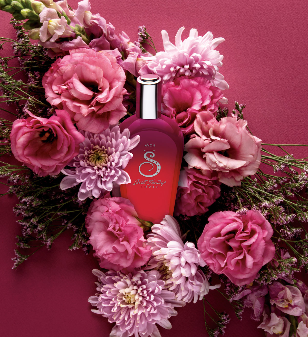 Frasco de fragancia rojo rodeado de flores rosas sobre fondo magenta