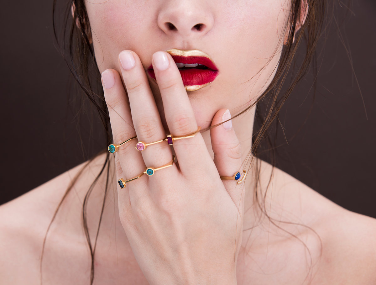 Primer plano de labios rojos y dedos con anillos de piedras de colores