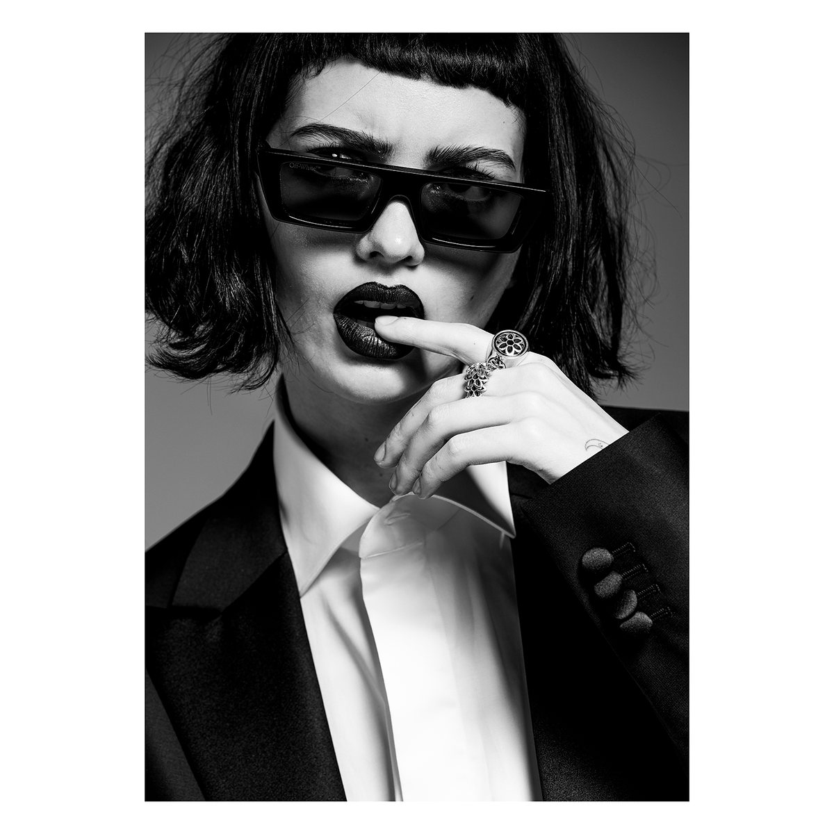 Black-and-white portrait of a model in sunglasses with a finger to her lips