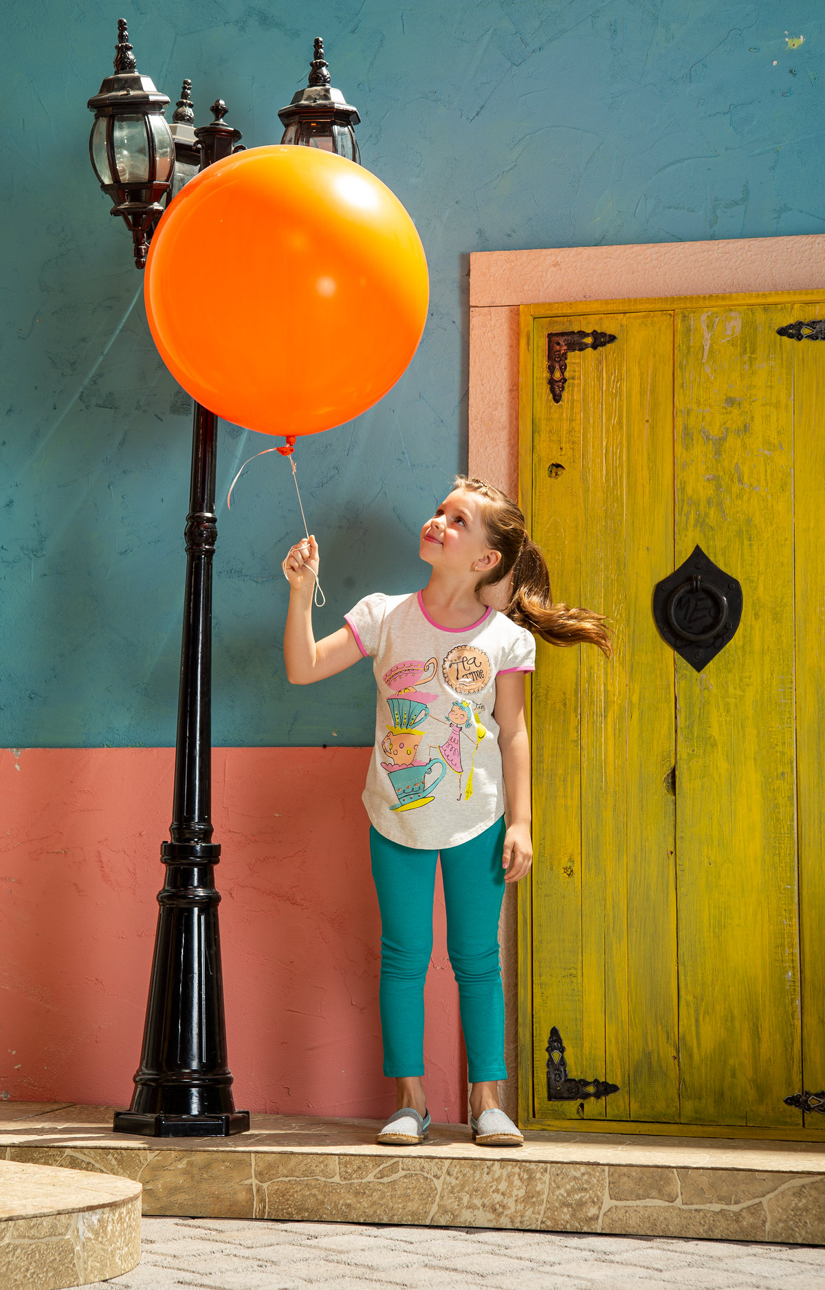 Niña con globo naranja frente a puertas de colores