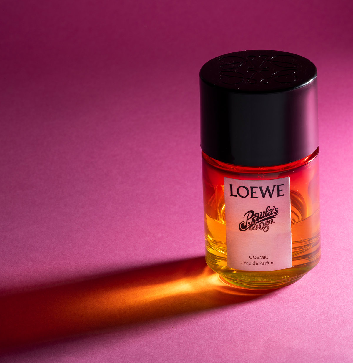 Frasco de perfume Loewe Paula's Ibiza sobre fondo magenta con reflejo naranja
