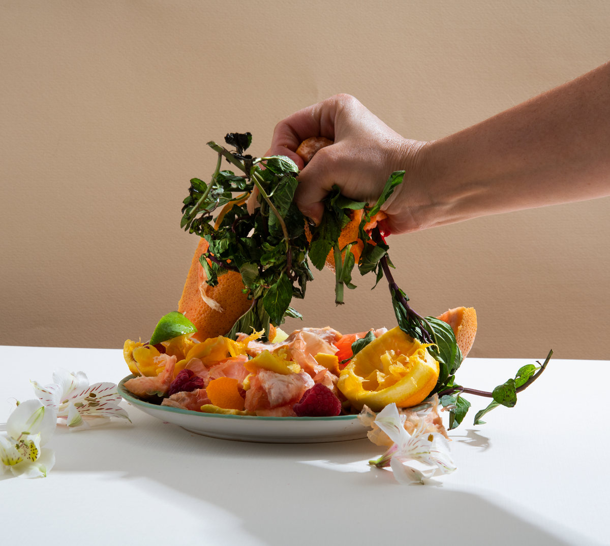A hand lifts herbs from a platter of fresh fruit on beige