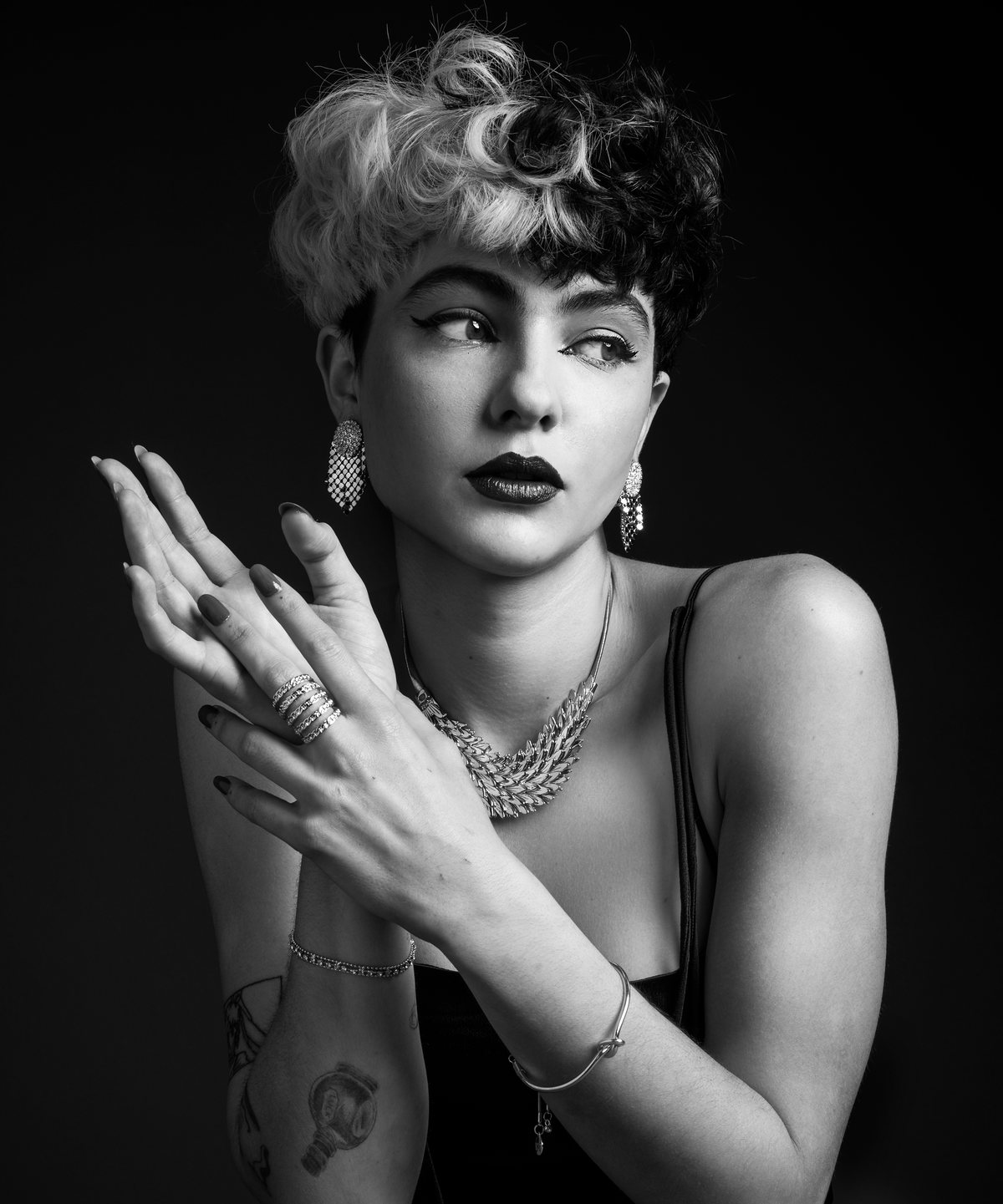 Black-and-white portrait of a curly-haired model with hands clasped, wearing jewelry
