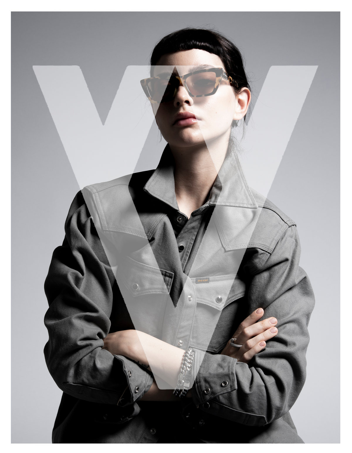 Retrato en blanco y negro de modelo con lentes oscuros y camisa de mezclilla, brazos cruzados, con logotipo de The Silver Deer