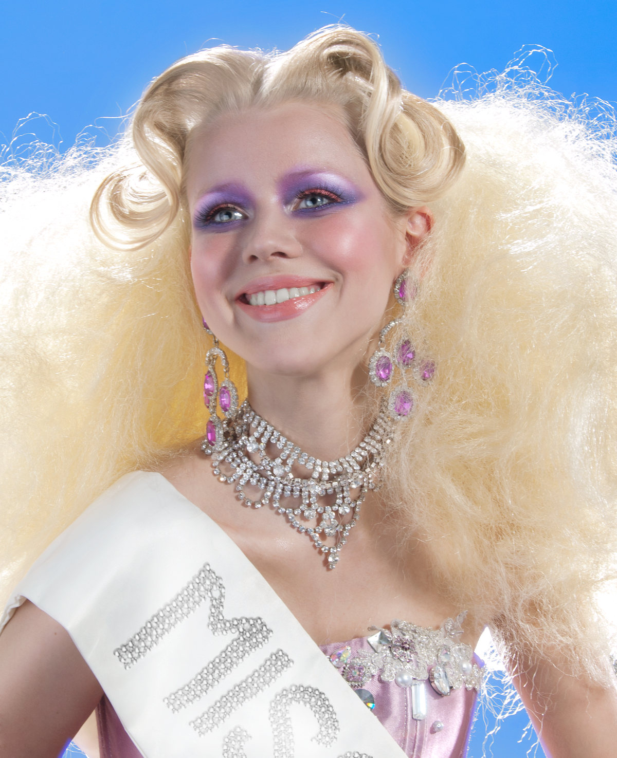 Model with a pageant sash, voluminous blonde hair and a crystal necklace on blue