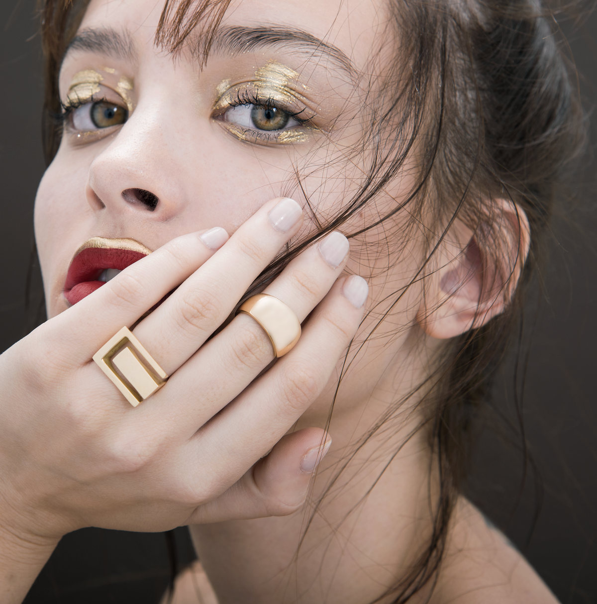Close-up of a model with gold eyeshadow, red lips and gold rings