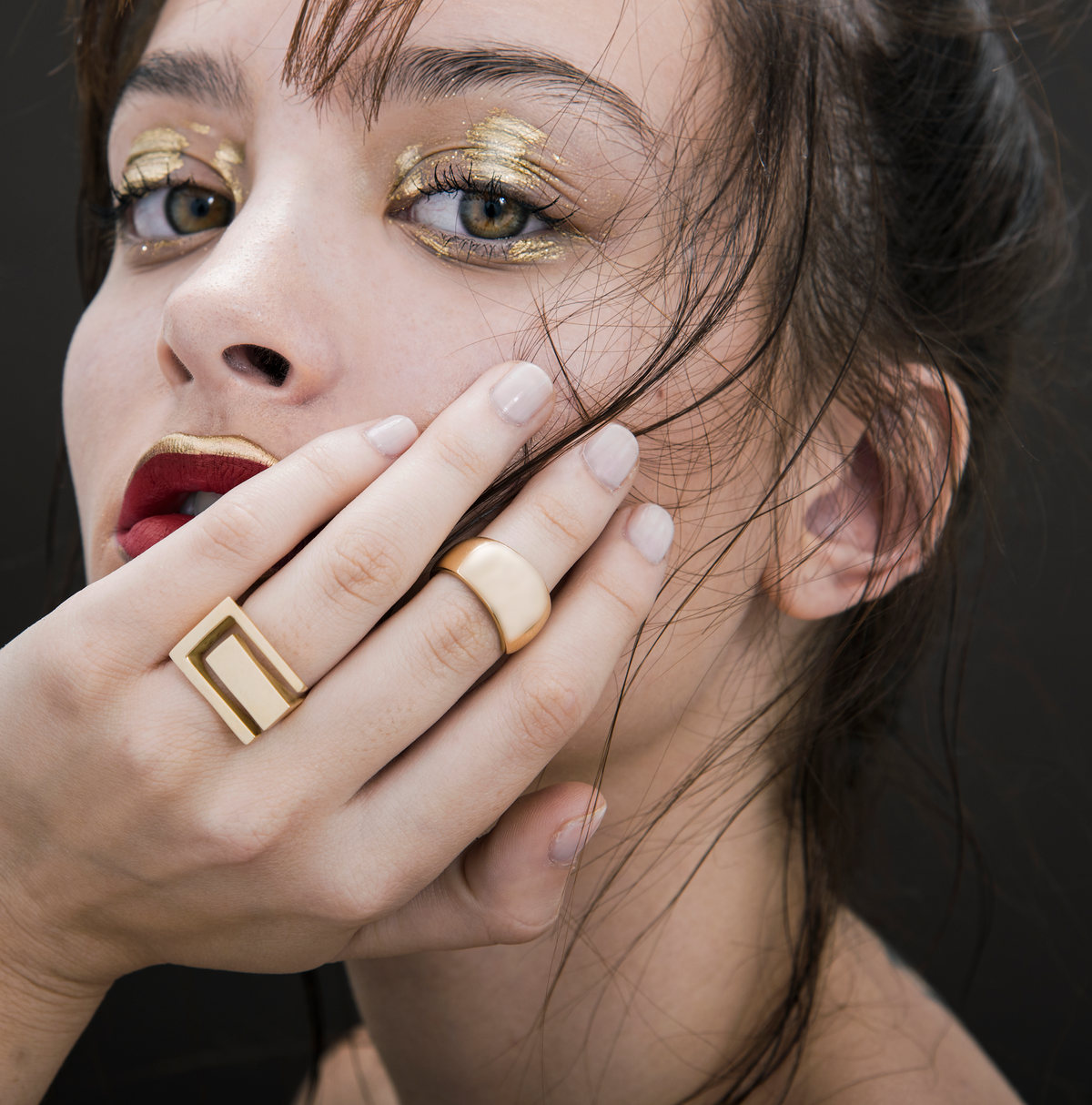 Primer plano de modelo con sombra dorada, labios rojos y anillos dorados