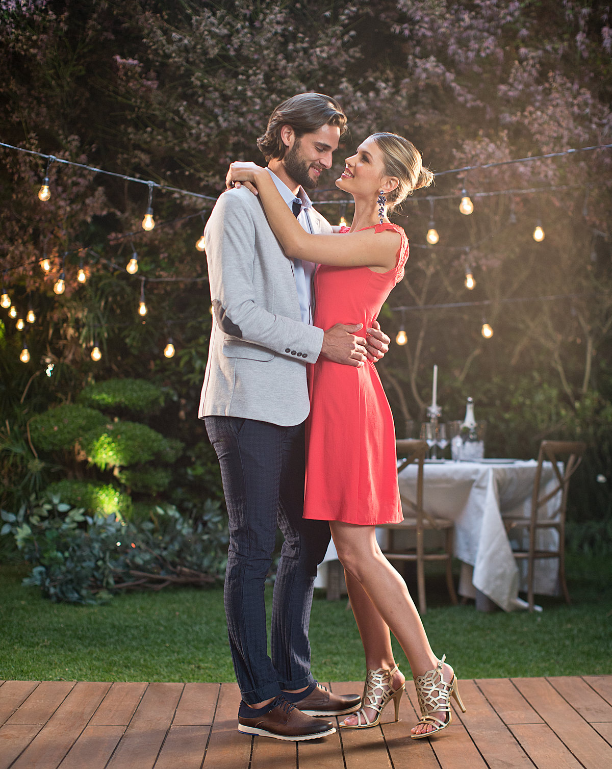 Pareja abrazada en un jardín de noche bajo luces colgantes