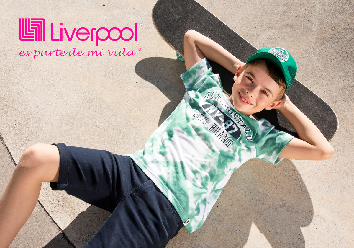 Niño con gorra y playera tie-dye recostado sobre una patineta, con logotipo de Liverpool