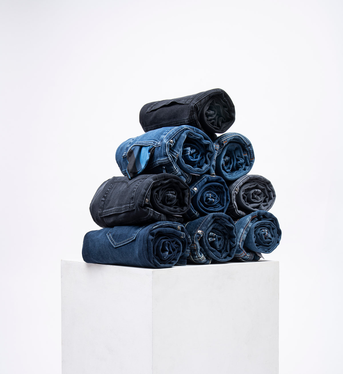 Jeans enrollados apilados en pirámide sobre un pedestal blanco