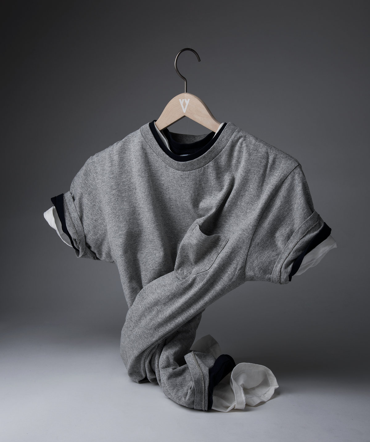 Playera gris colgada de un gancho, con la tela en movimiento, fondo gris