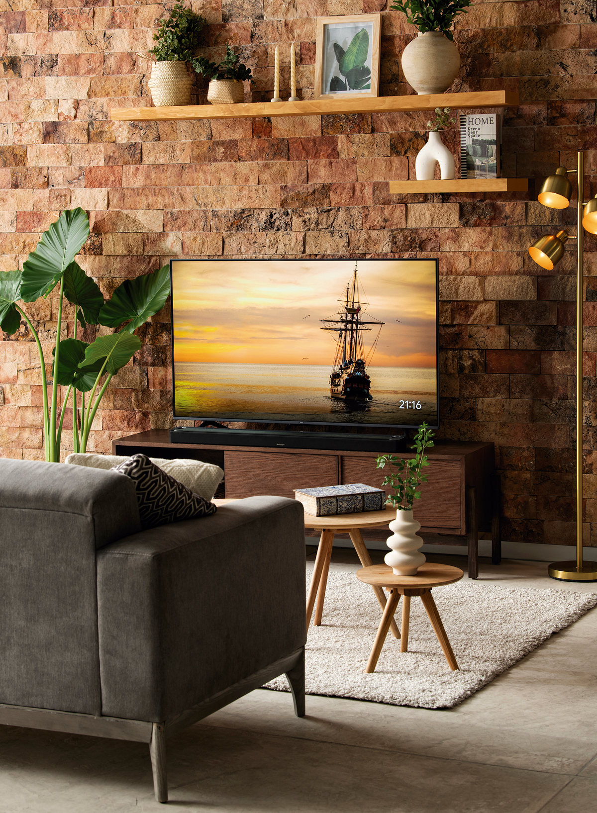 Living room with a brick wall, TV, gray sofa and plants