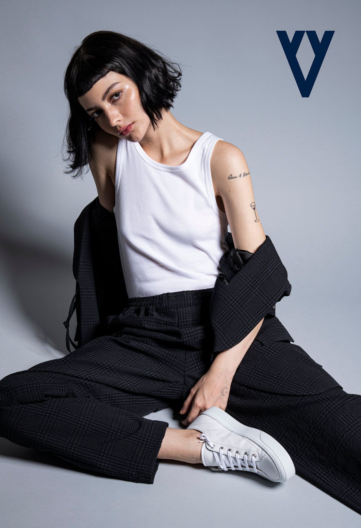 Modelo de cabello corto con camiseta blanca, pantalón negro y tenis, sentada sobre fondo gris, con logotipo de The Silver Deer
