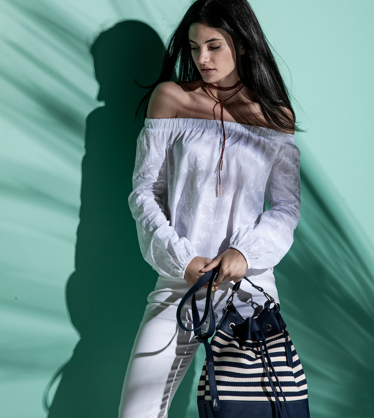 Modelo con blusa blanca de hombros descubiertos y bolso a rayas entre sombras de palmas