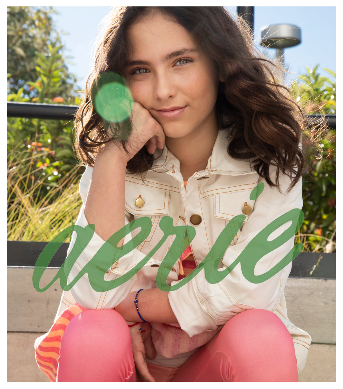 Joven sonriente con chamarra clara y pantalón rosa, con logotipo de Aerie