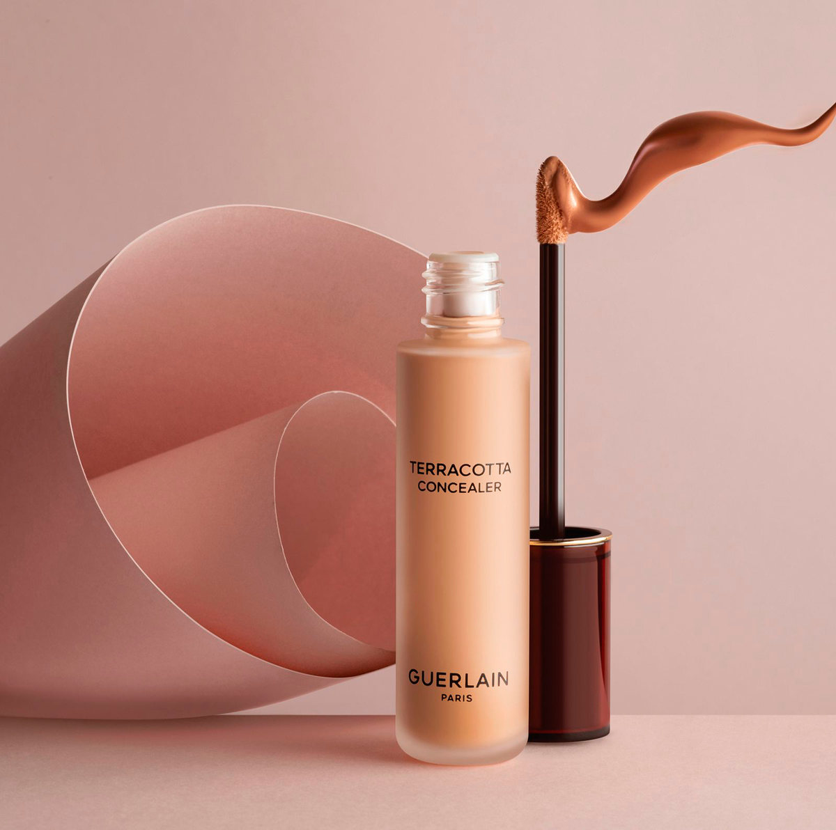 Corrector Guerlain Terracotta con un trazo de producto sobre fondo rosa