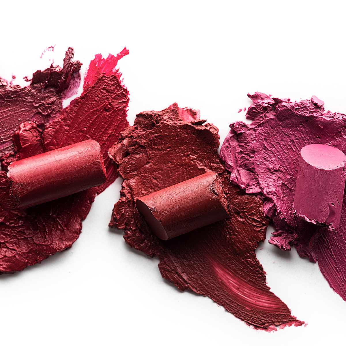 Red and pink lipstick bullets smeared across a white surface