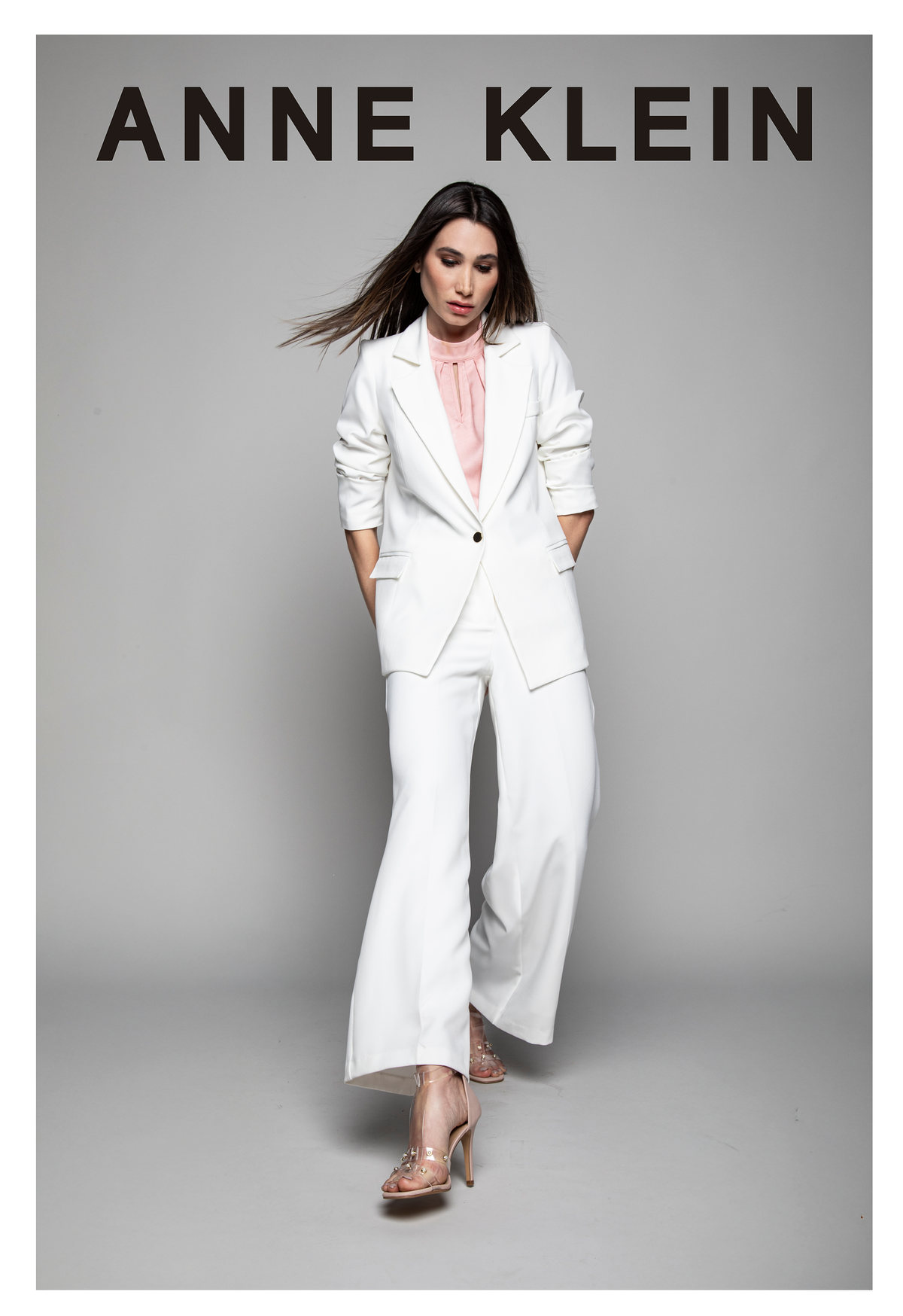 Modelo con traje sastre blanco sobre fondo gris, con logotipo de Anne Klein